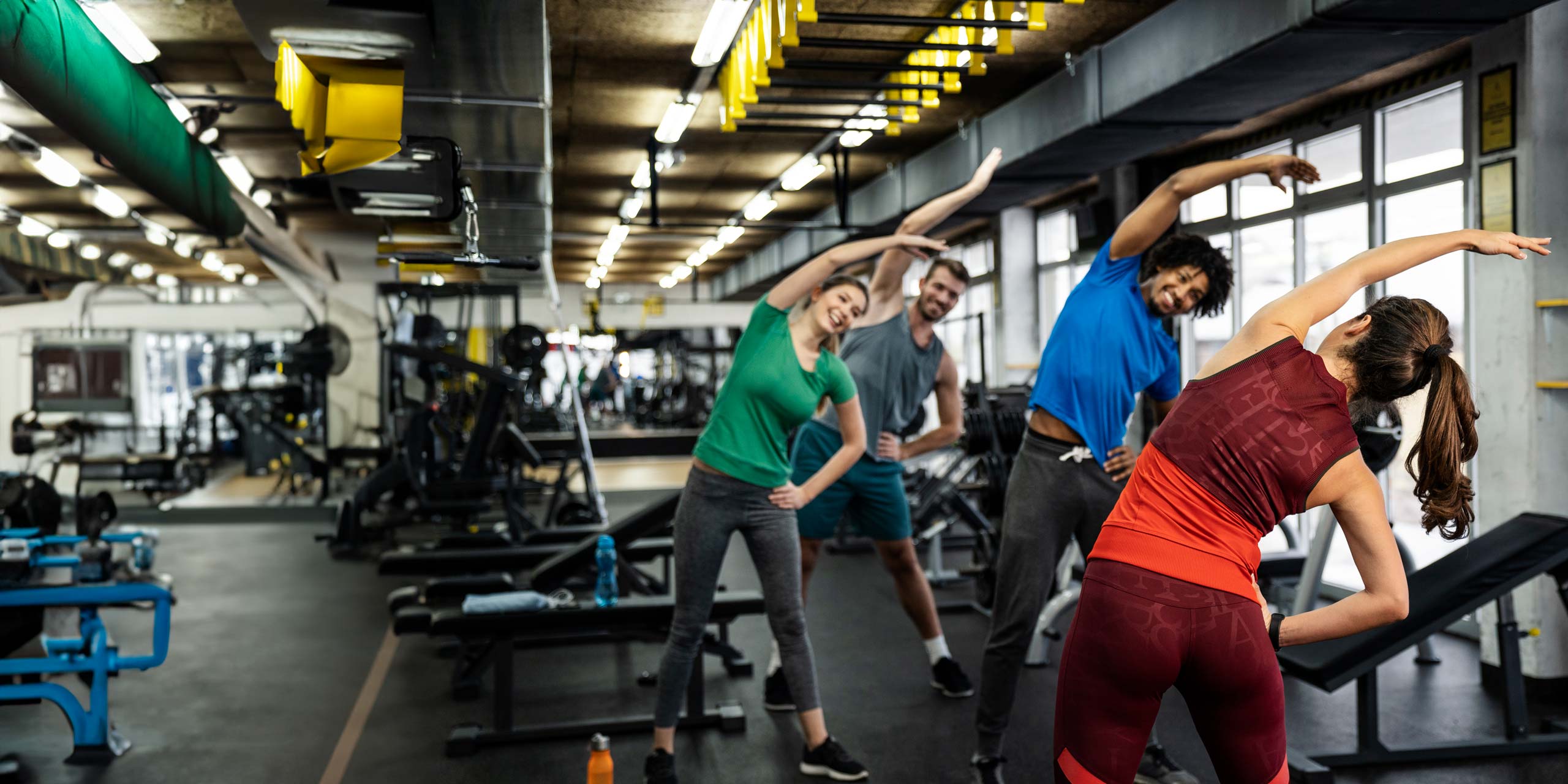 2 Männer und 2 Frauen machen Dehnübungen im Fitnessstudio