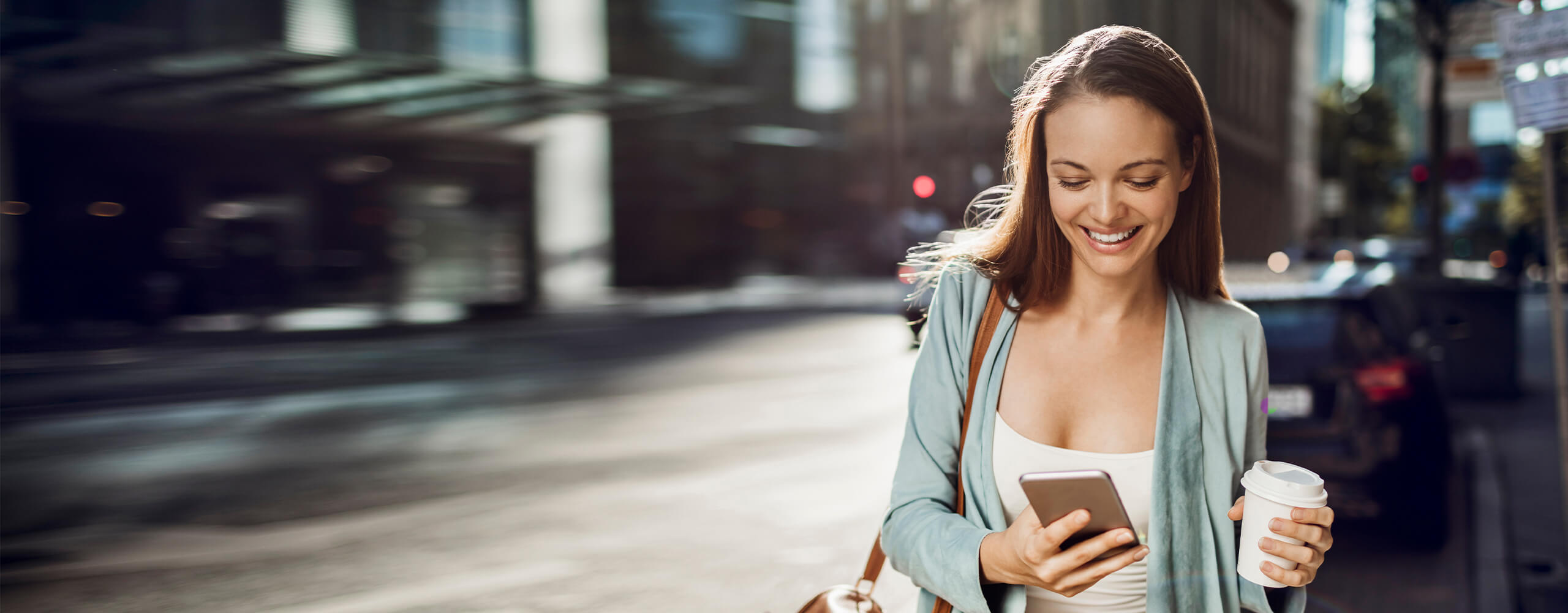 Junge Frau geht eine Straße entlang und schaut dabei auf ihr Smartphone